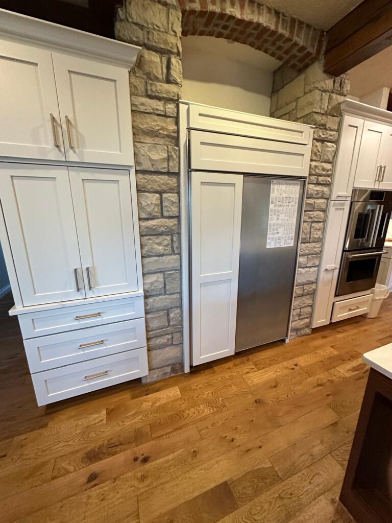 Custom white kitchen cabinets with a built-in refrigerator surround integrated into a natural stone archway.