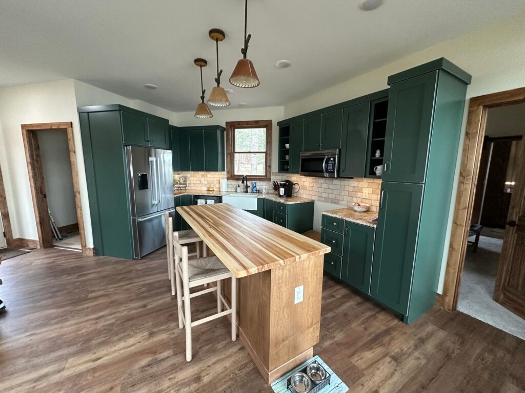 Custom white oak kitchen cabinets with a large marble island, black range hood, and natural stone wall by Max Craft.
