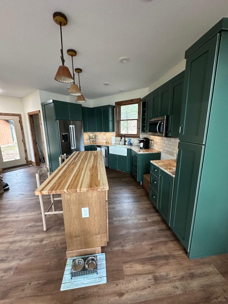 Custom white oak kitchen cabinets with a large marble island, black range hood, and natural stone wall by Max Craft.