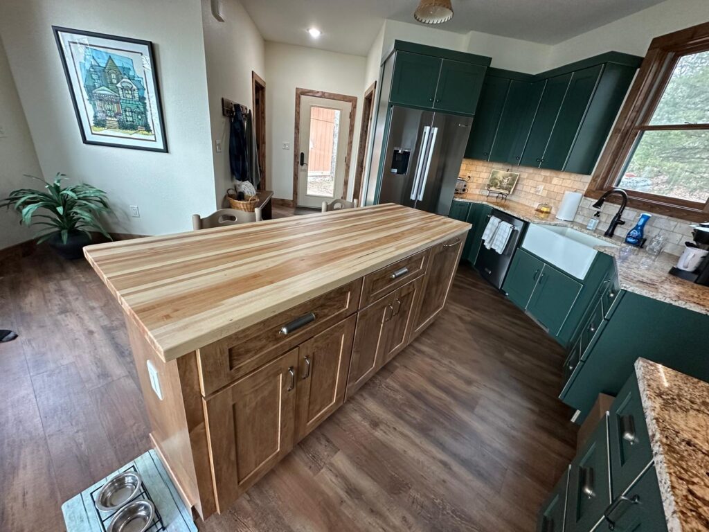 Custom white oak kitchen cabinets with a large marble island, black range hood, and natural stone wall by Max Craft.