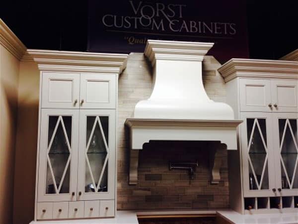 An architectural luxury kitchen design highlighted by a custom dark-stained D-Series wood range hood featuring sweeping lines, classic corbels, and a custom-scaled chimney.